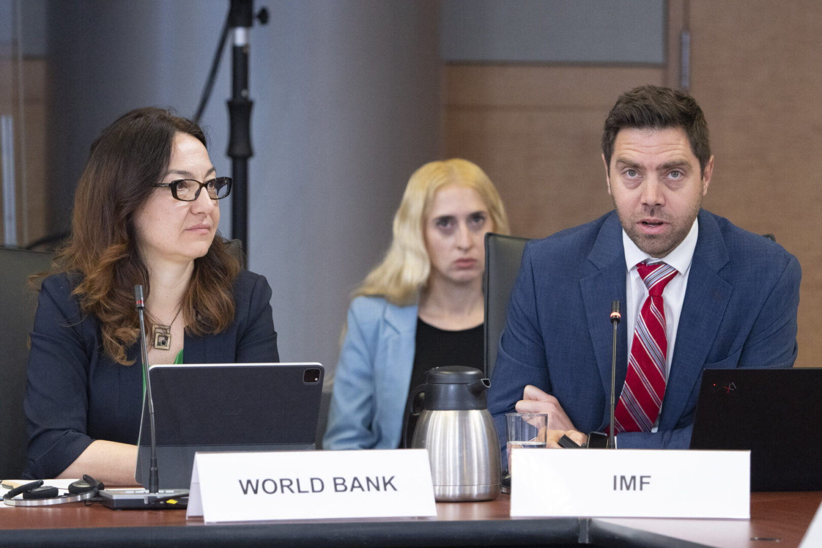 Three people at a conference table, IMF sign.